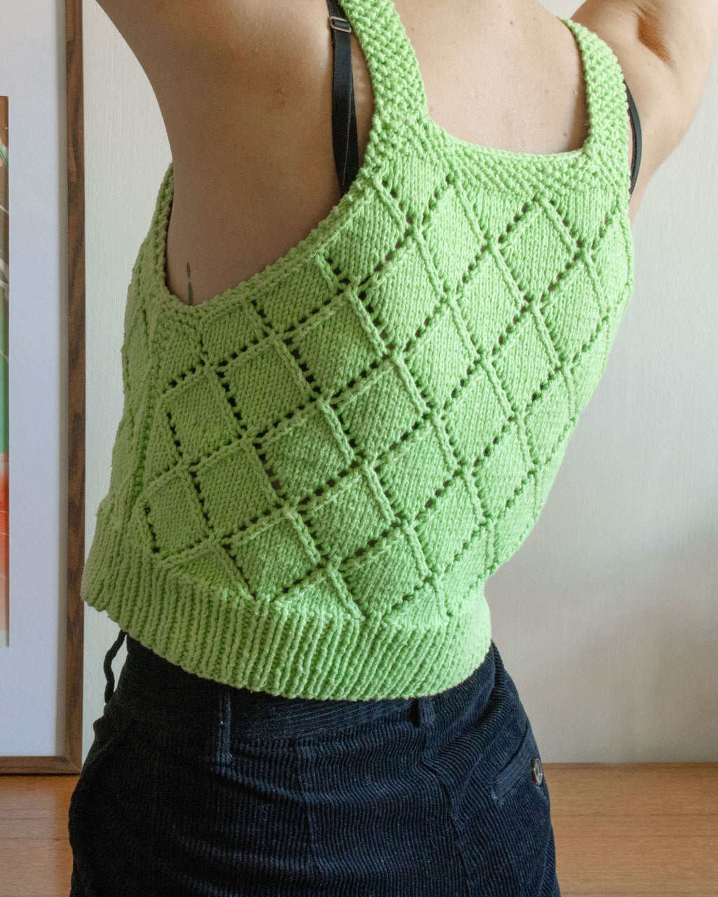 Close up of the back of a person wearing a green knitted vest top in front of a white wall