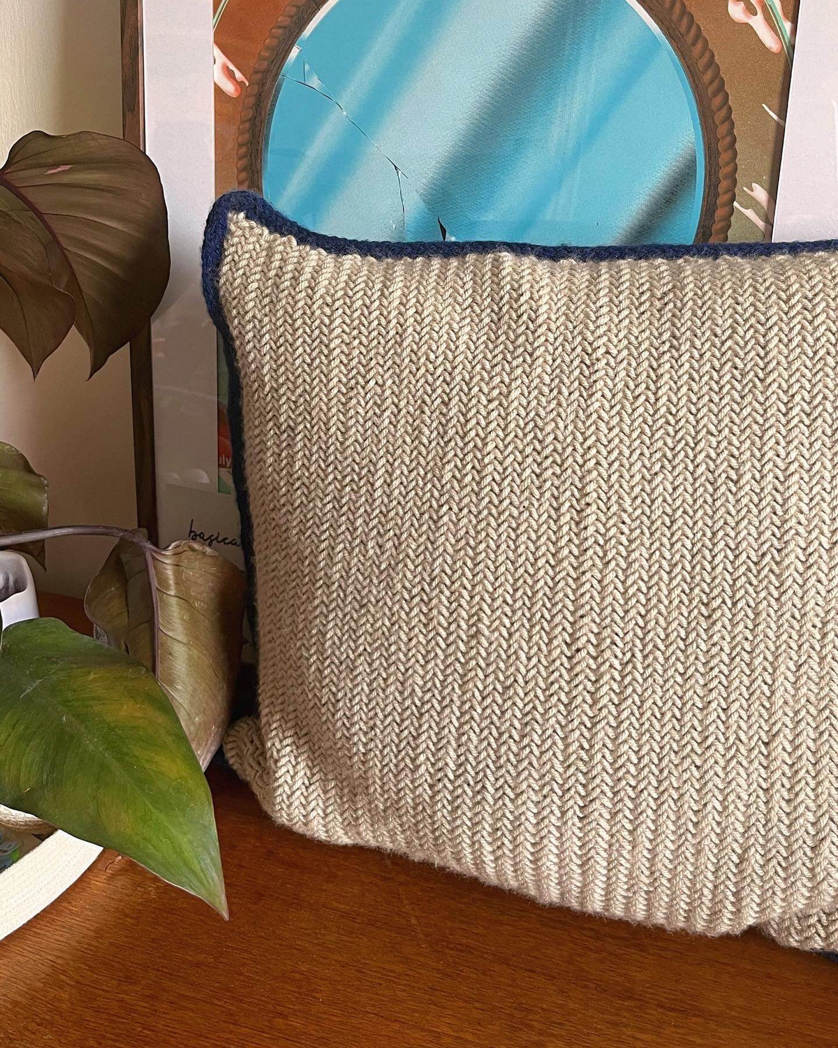 Beige herringbone stitch pillow with blue trim on a wooden surface